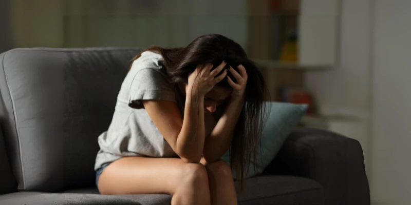 Teen girl sitting on a couch with her head in her hands, displaying signs of anxiety and stress.